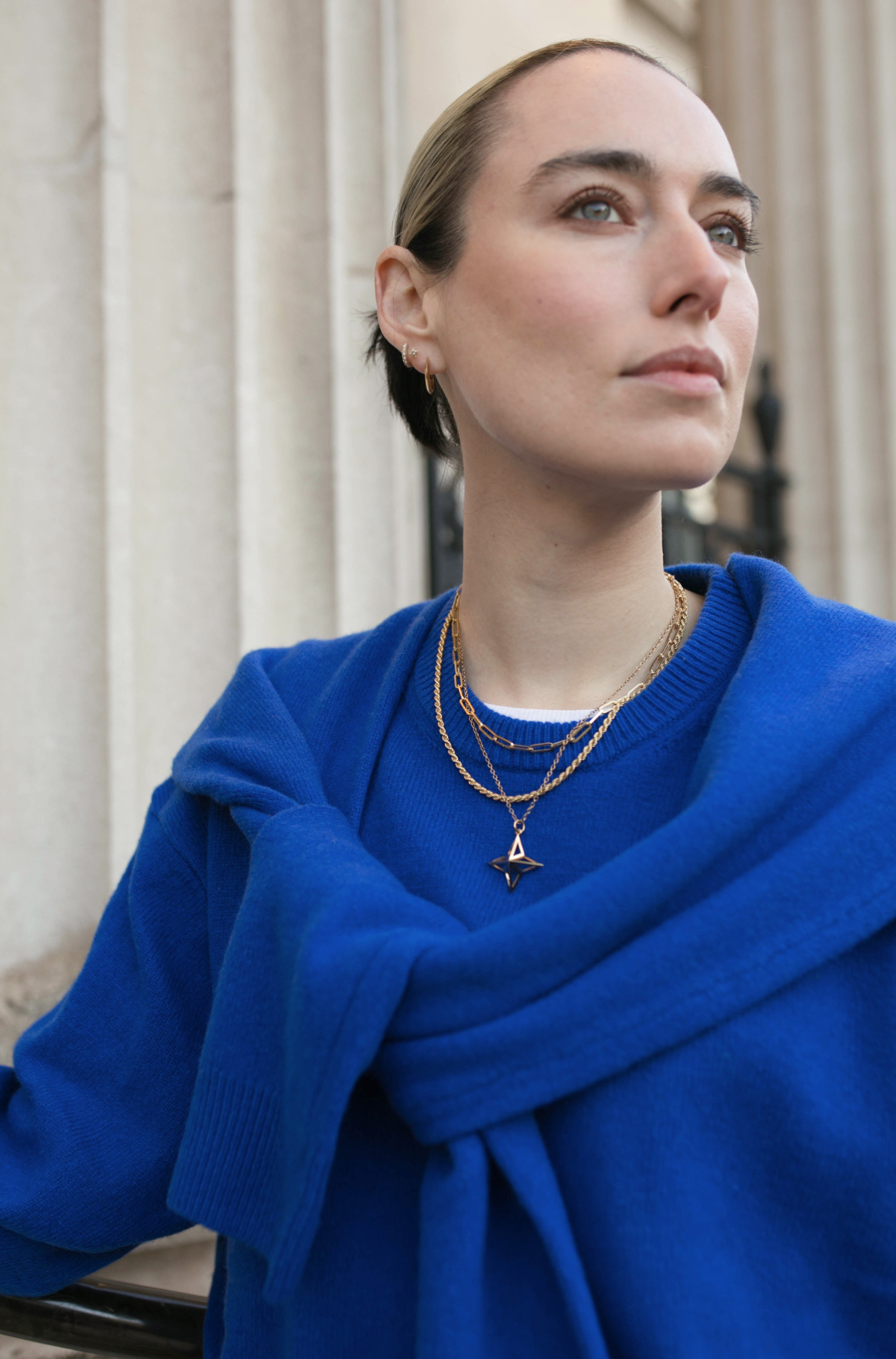 Close up of model in front of fluted columns wearing an assortment of Antonia Guise Gold Vermeil Jewellery