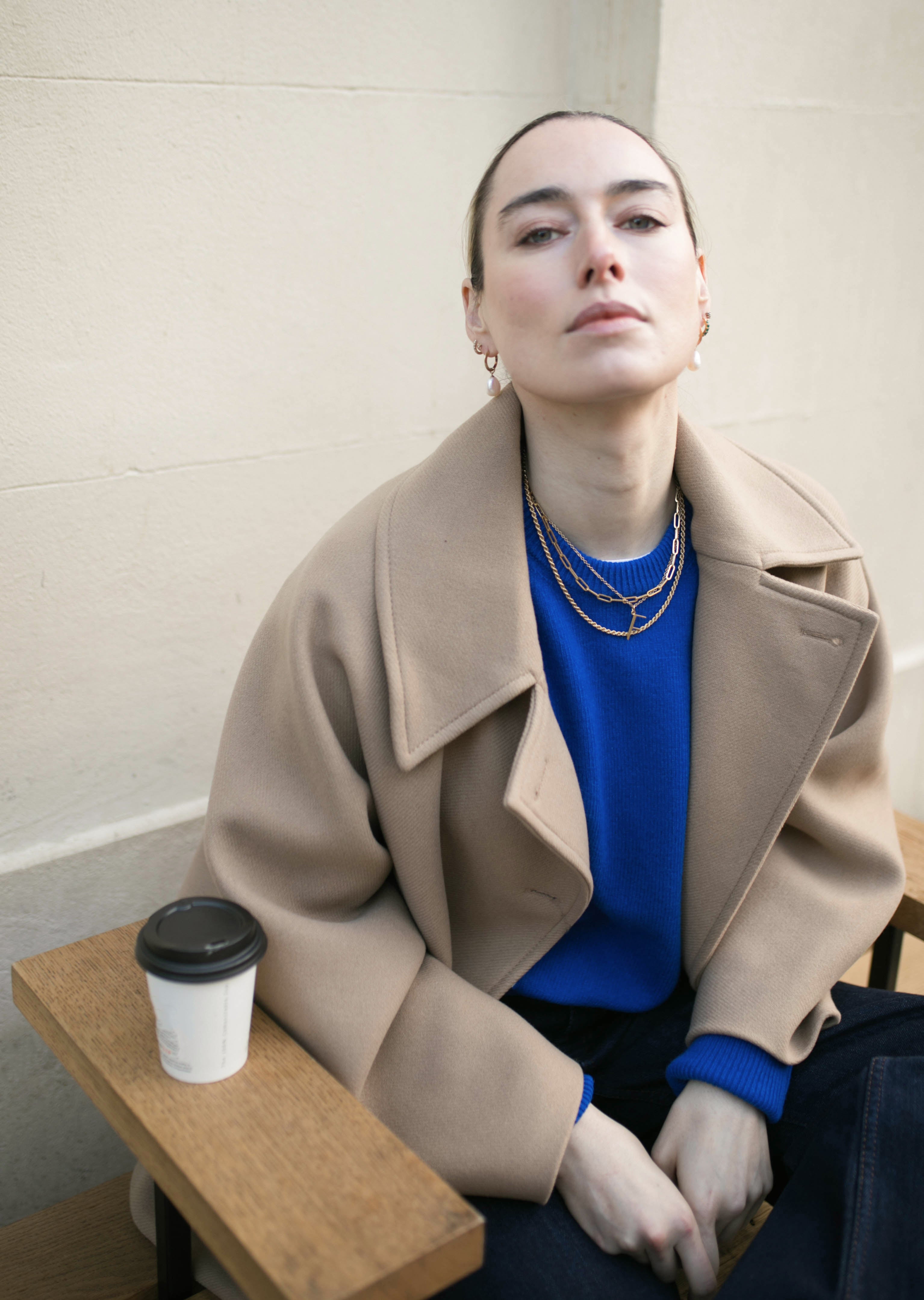 Model wearing blue jumper looking to camera wearing our Hedy Pearl Drops whilst enjoying a coffee