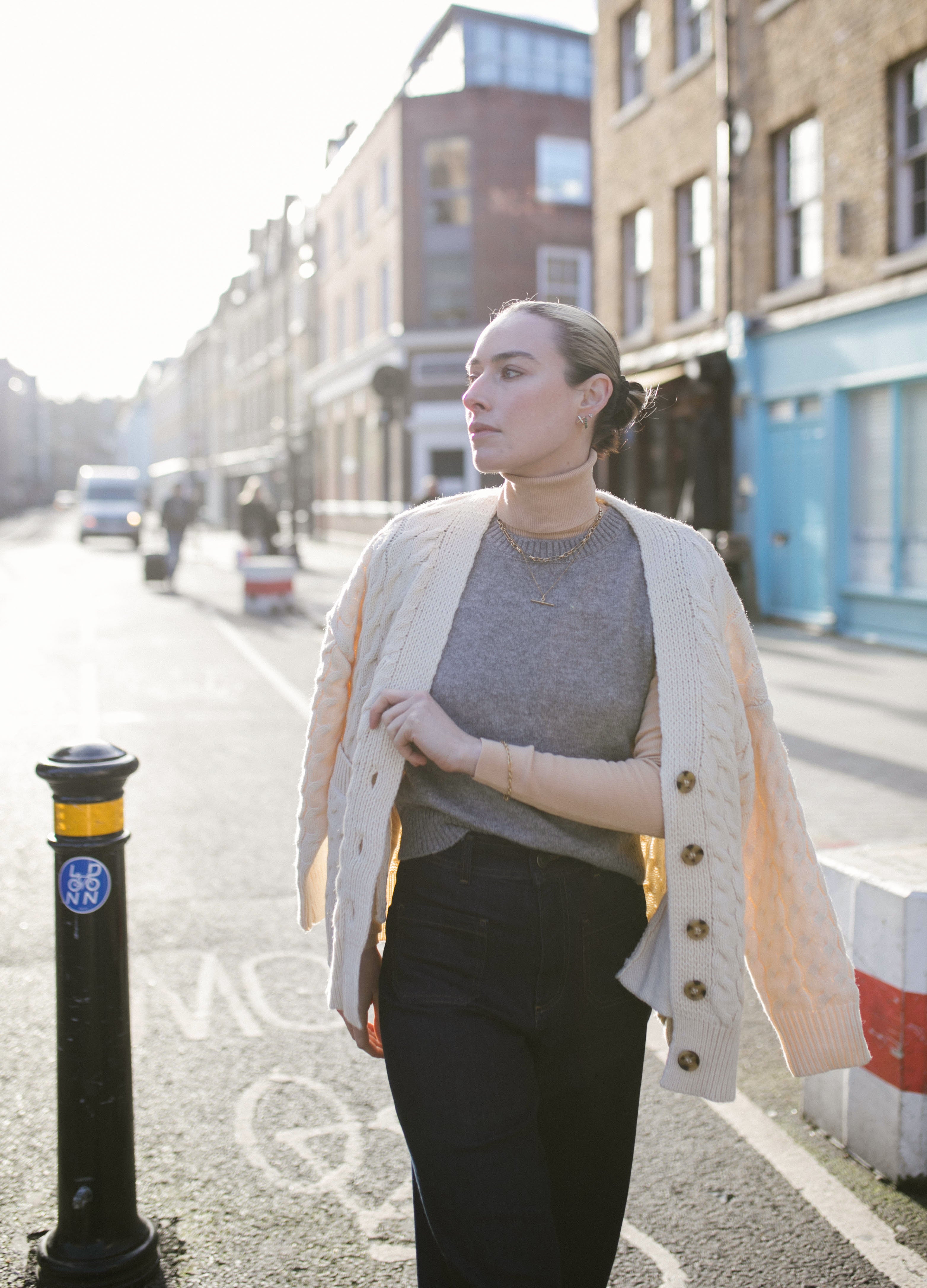 Our Model walking towards camera on bermondsey Street wearing a white cardi and grey vest plus a selection of Antonia Guise gold vermeil Jewellery