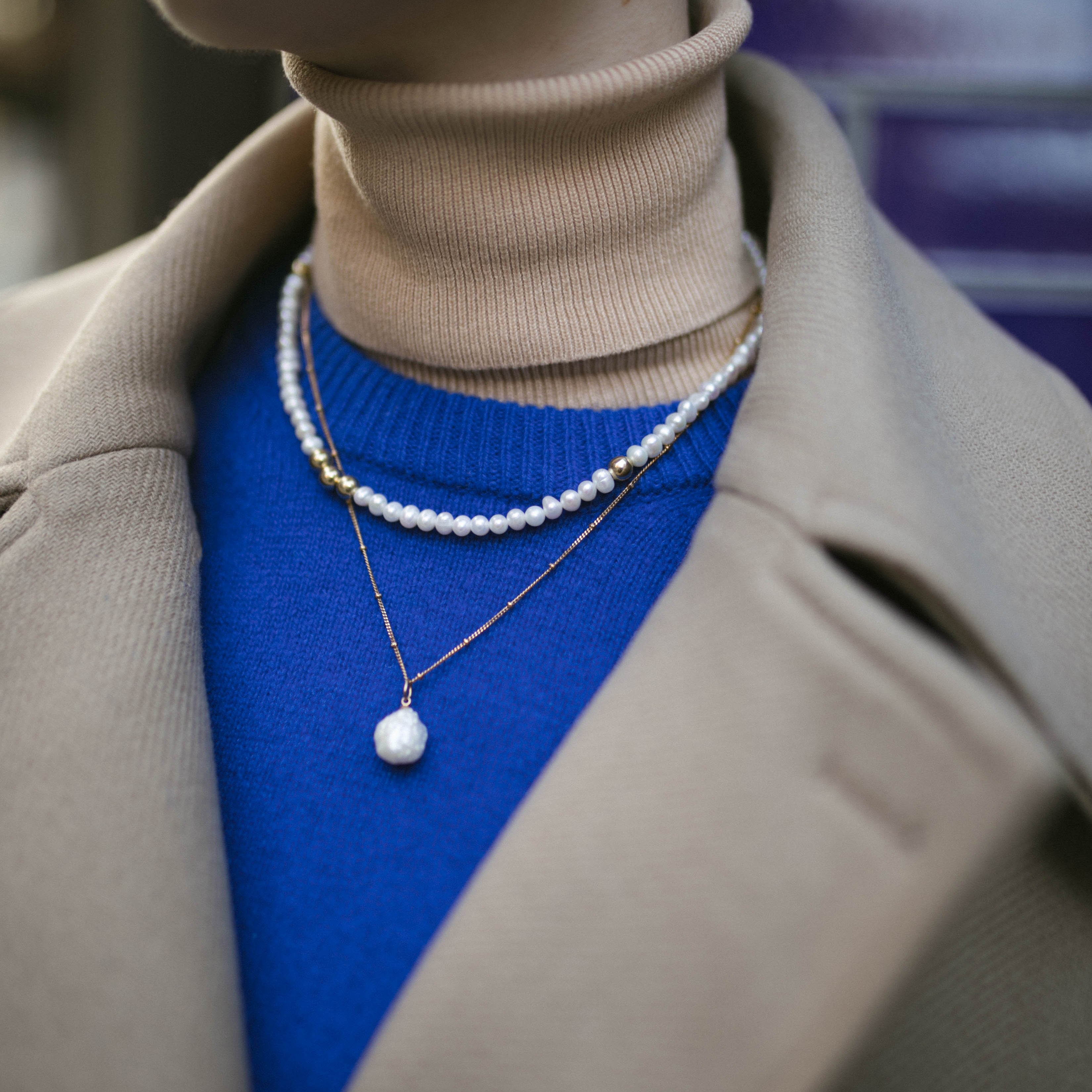 Model wearing blue jumper and camel coat along with our Anna Pearl Necklace and Grace Pearl Necklace