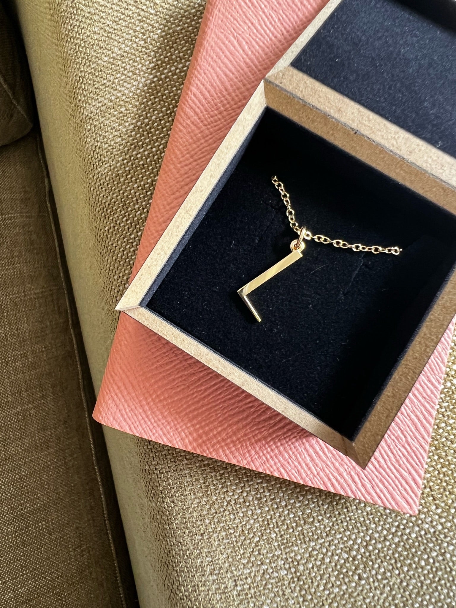 L initial necklace on a white background with shadows and mustard velvet ribbon snaking around it