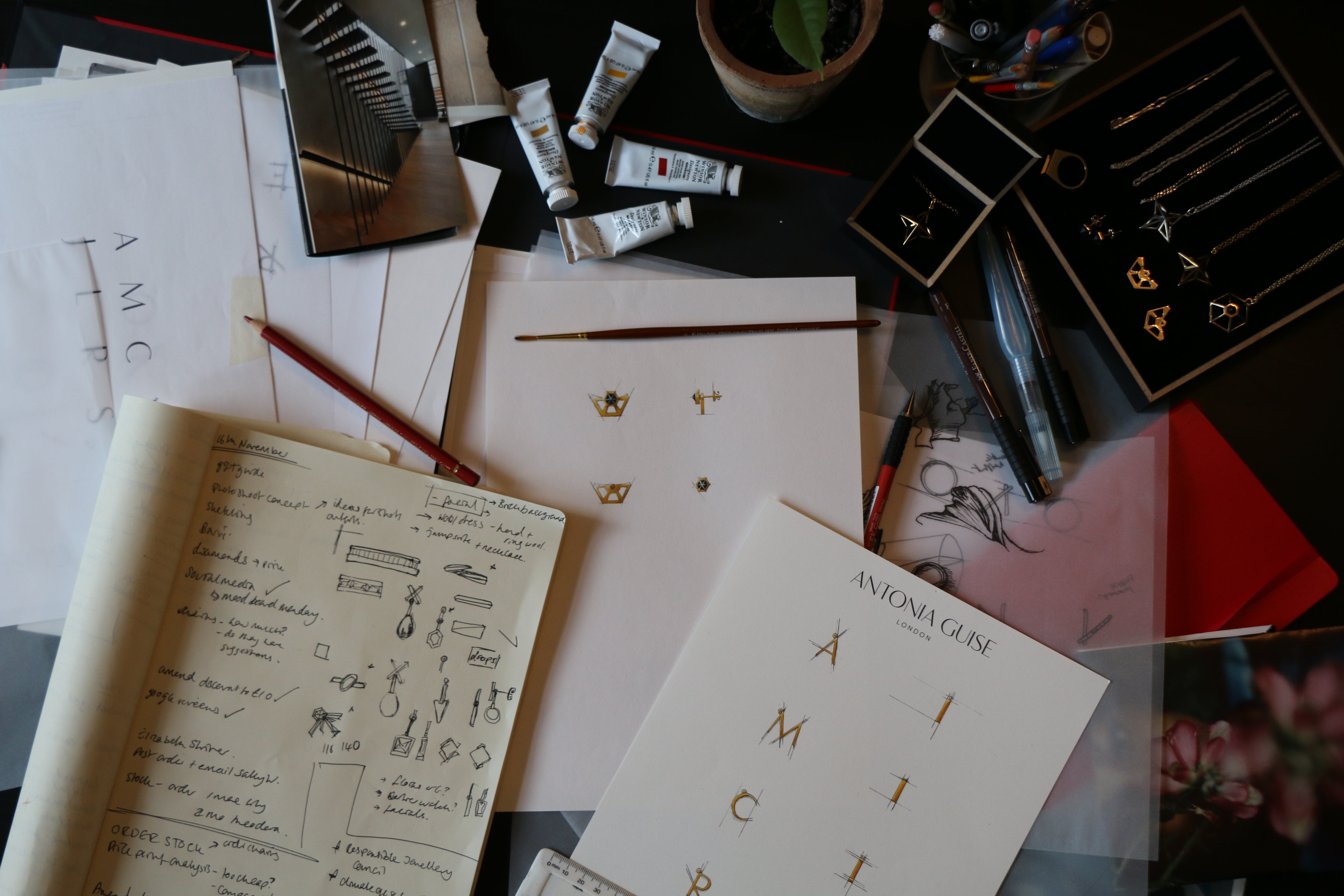 A shot of Antonia's design desk featuring the hand painted designs for our Anne Initial Necklaces plus note book