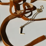 L initial necklace on a white background with shadows and mustard velvet ribbon snaking around it
