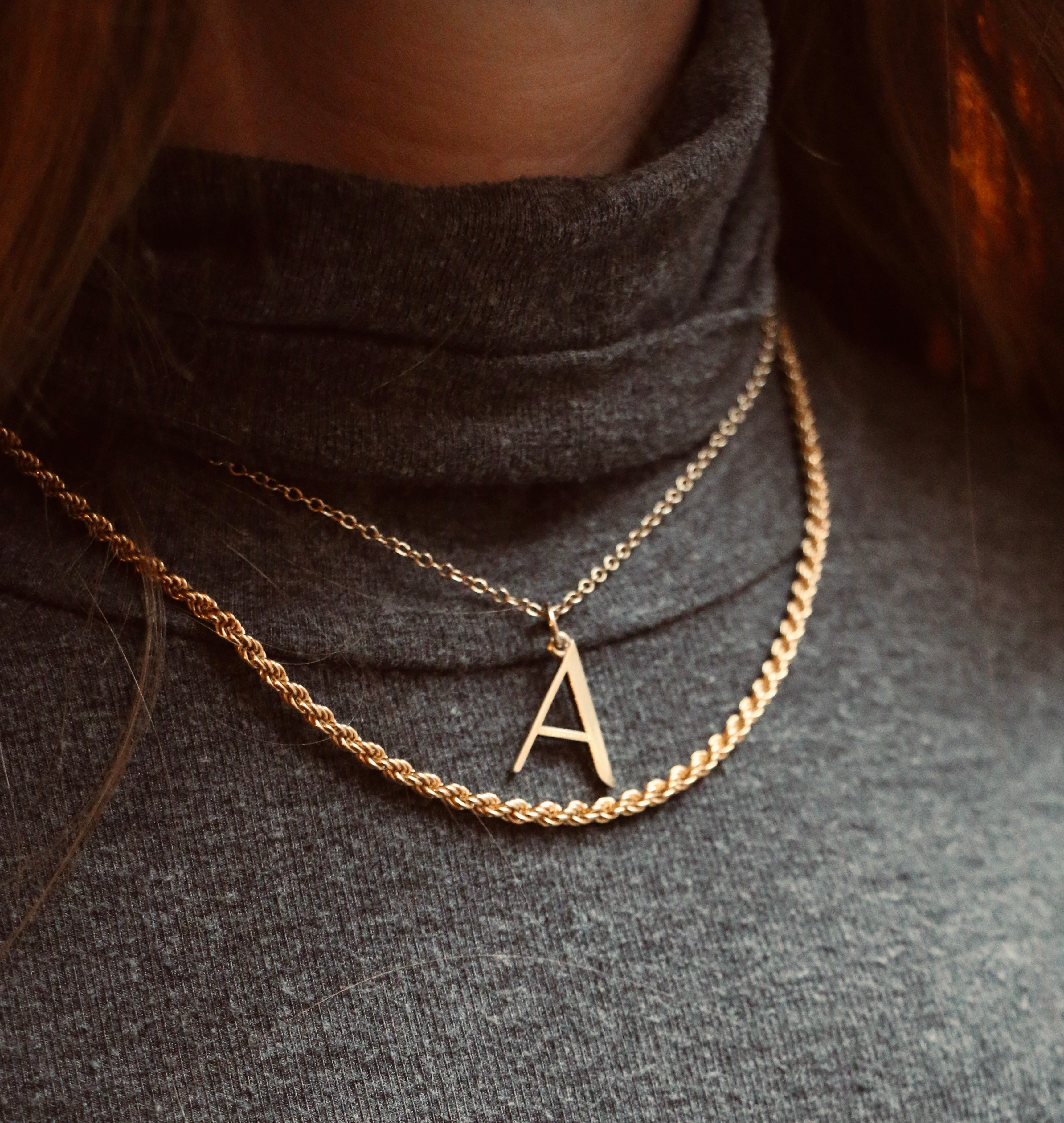 A Anne Initial Necklace worn with Rosalind Chain on a model wearing a grey top