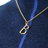 Close up of B Necklace worn by a model wearing a blue jumper with a stripe down the middle of it