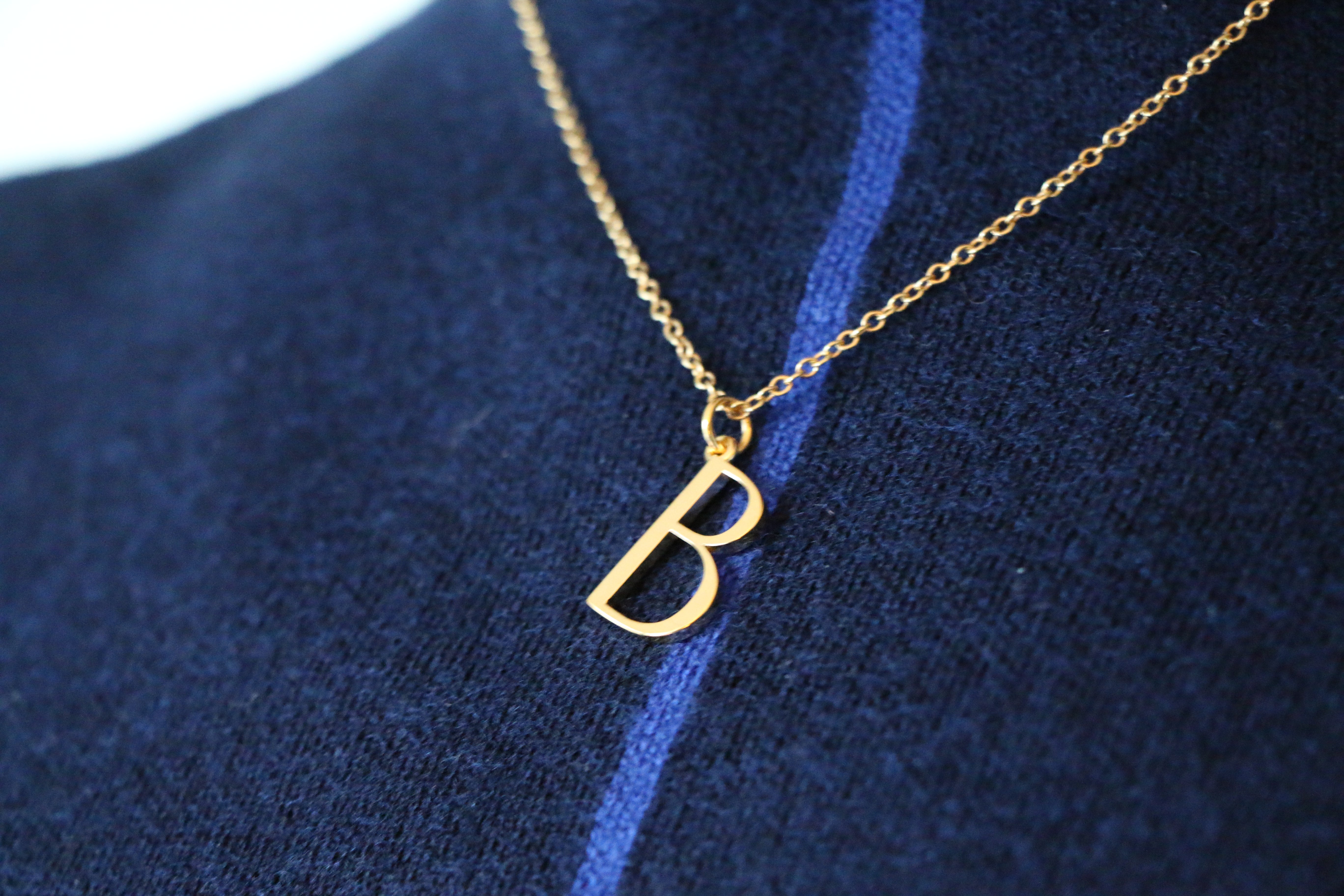 Close up of B Necklace worn by a model wearing a blue jumper with a stripe down the middle of it