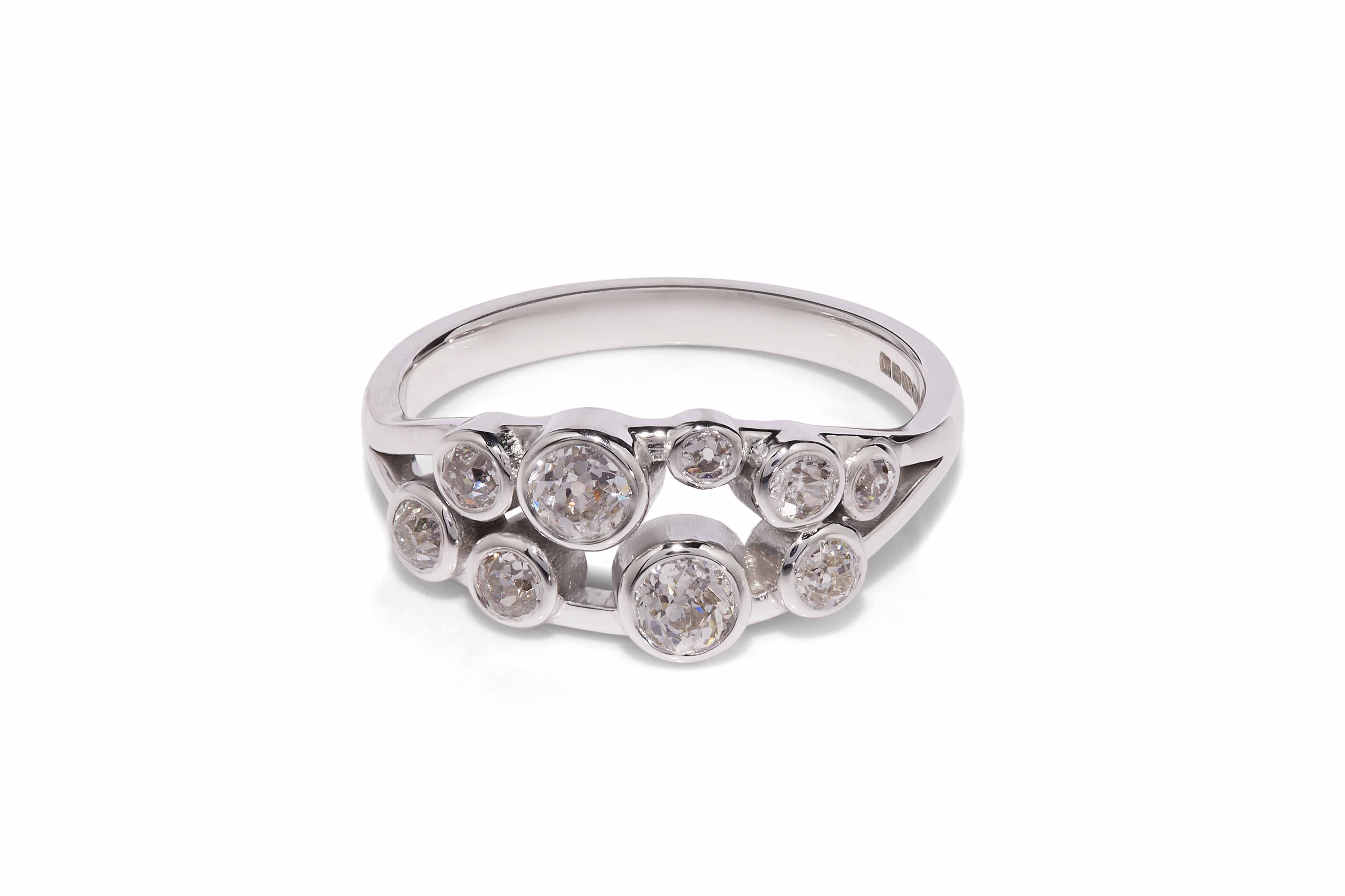 Multi-stone, bezel set diamond ring with split band made in platinum lying on white background with shadow