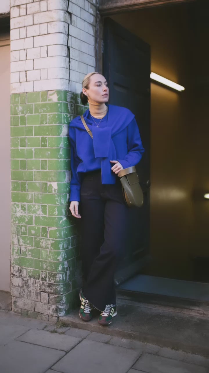 Video showing our model in a royal blue jumper and jeans leaning against a wall wearing a selection of Antonia Guise Gold Chains