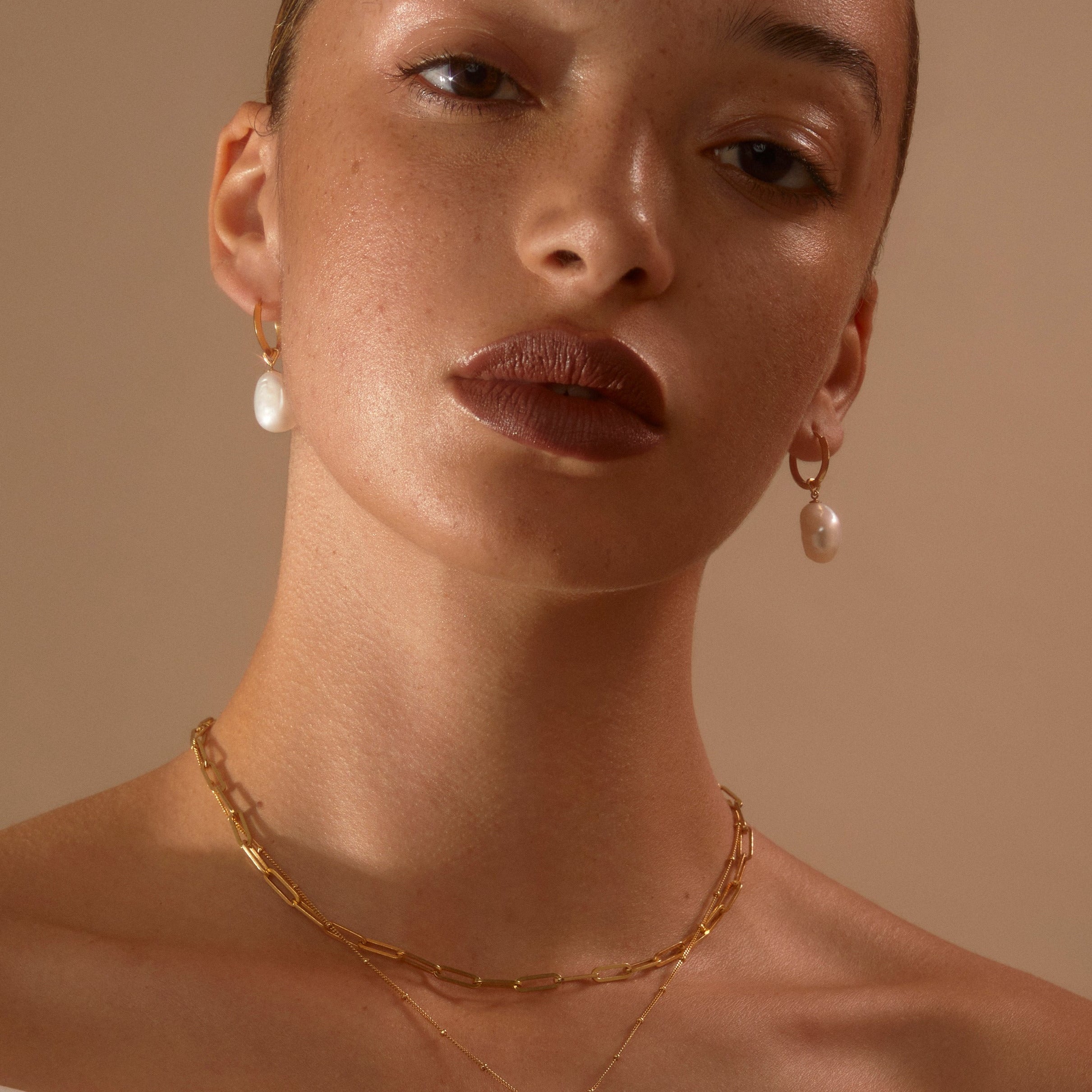 Model wearing our Gold Cecilia Huggie Hoops with our Pearl Drops looking to camera