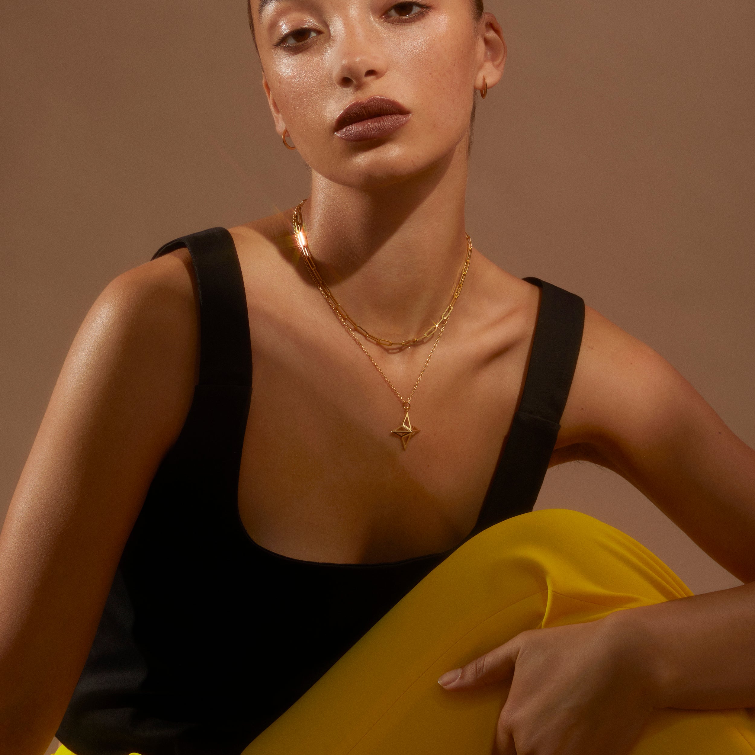 Model looking to camera wearing banana yellow trousers and a black top with the Antonia Guise Theodora necklace in gold vermeil and out Jenny Trace Chain