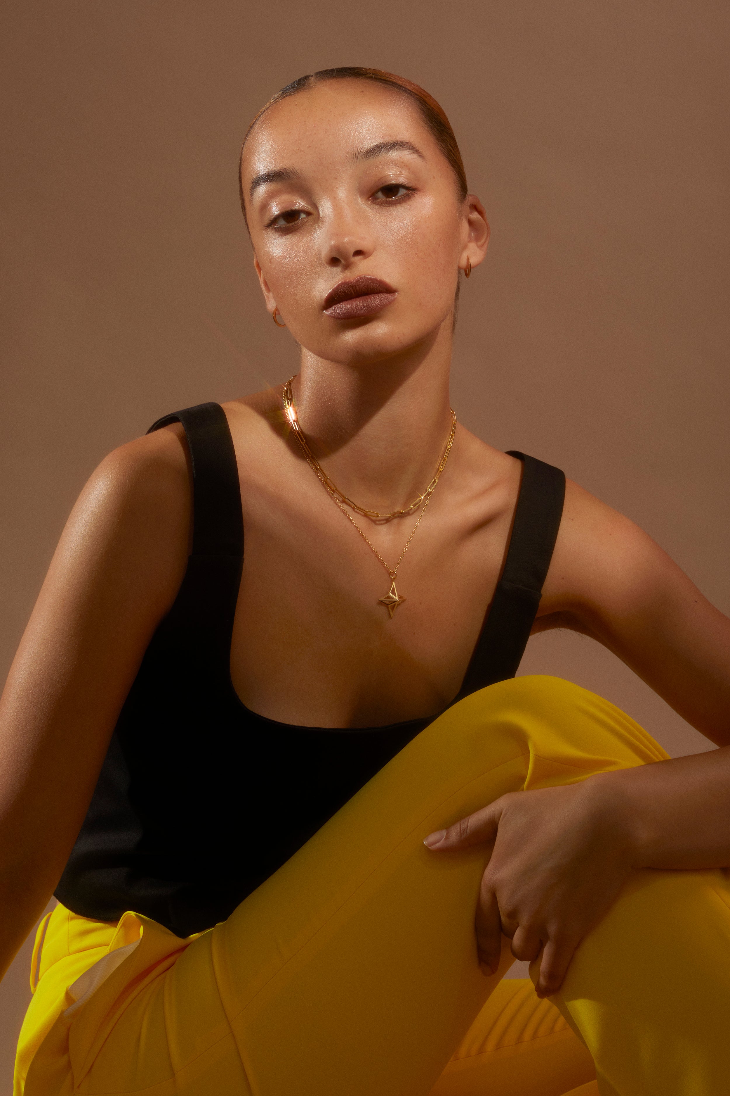 Model looking to camera wearing banana yellow trousers and a black top with the Antonia Guise Theodora necklace in gold vermeil and out Jenny Trace Chain