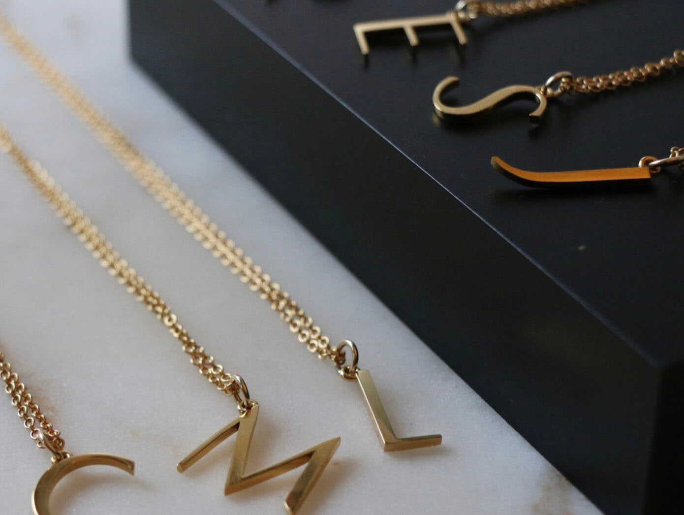 Close up of several anne initial necklaces, some on a white background others lifted up on a black platform