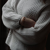 Model wearing white knit jumper and jeans with crossed arms and our Nancy Chain Bracelet made of recycled silver plated in gold