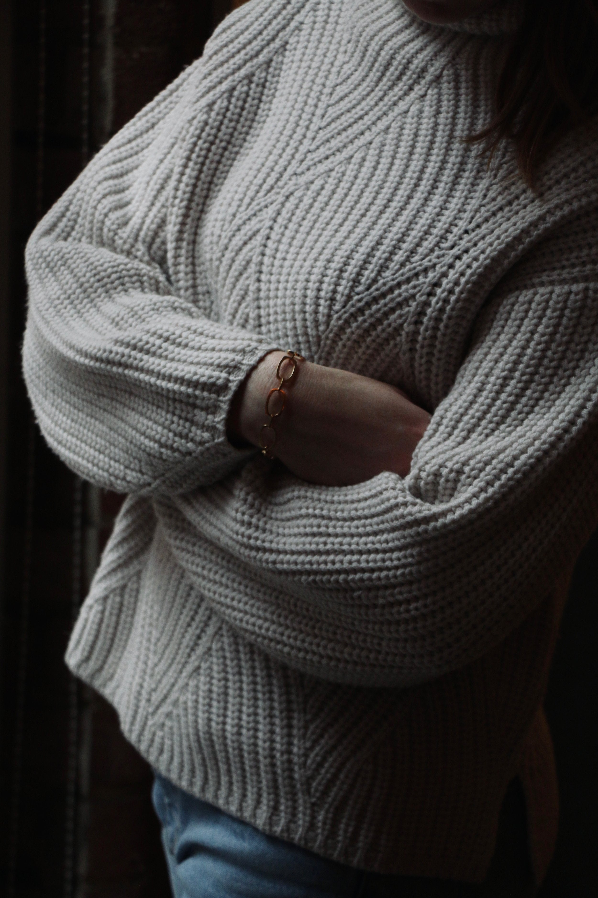 Model wearing white knit jumper and jeans with crossed arms and our Nancy Chain Bracelet made of recycled silver plated in gold