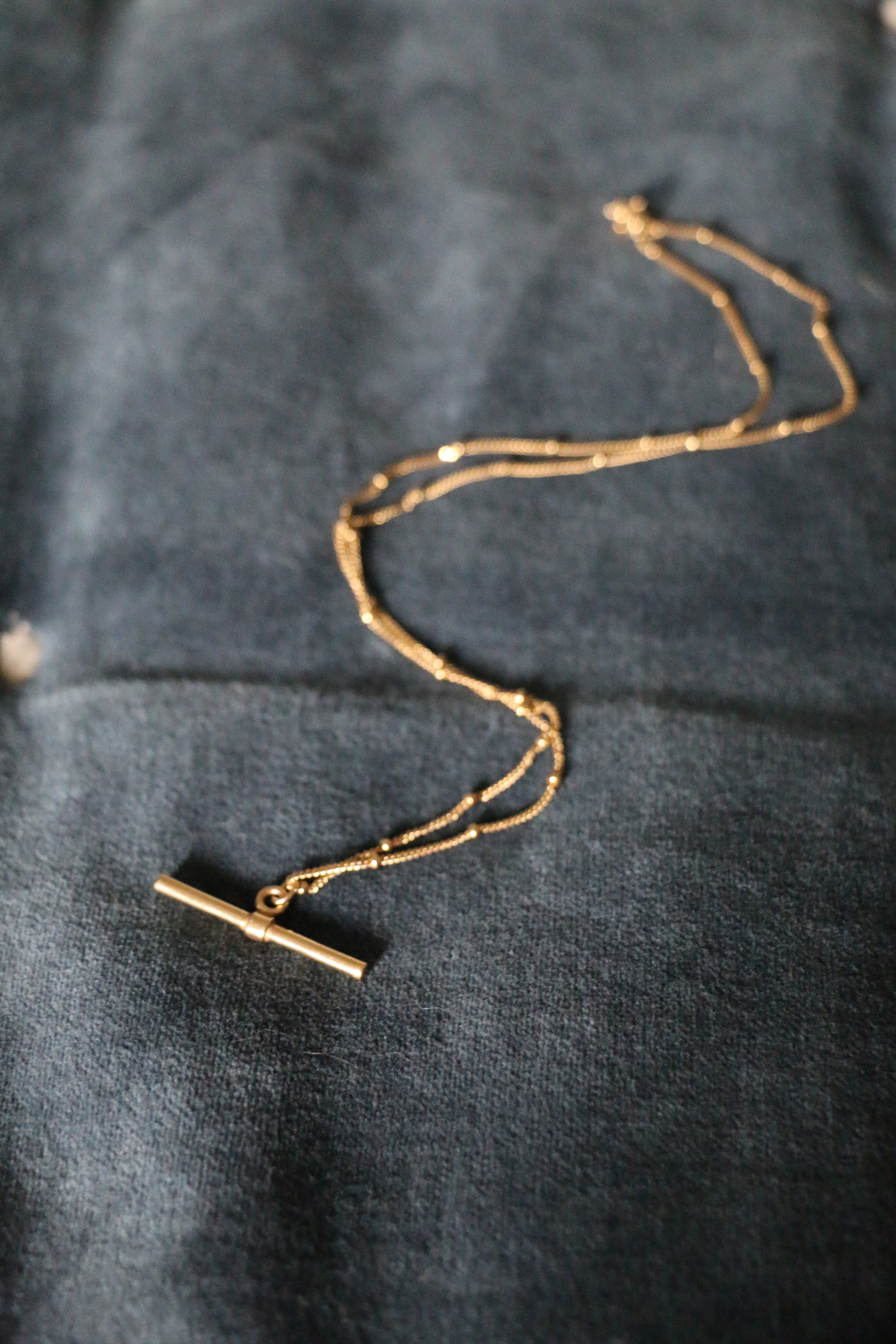 Our handmade in England, Gold Vermeil T-Bar Necklace lying on a blue velvet background