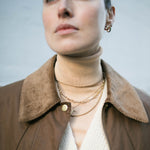 Model looking past camera wearing collared wax jacket and layered Antonia Guise gold vermeil necklaces including our Mary Figaro Chain Necklace