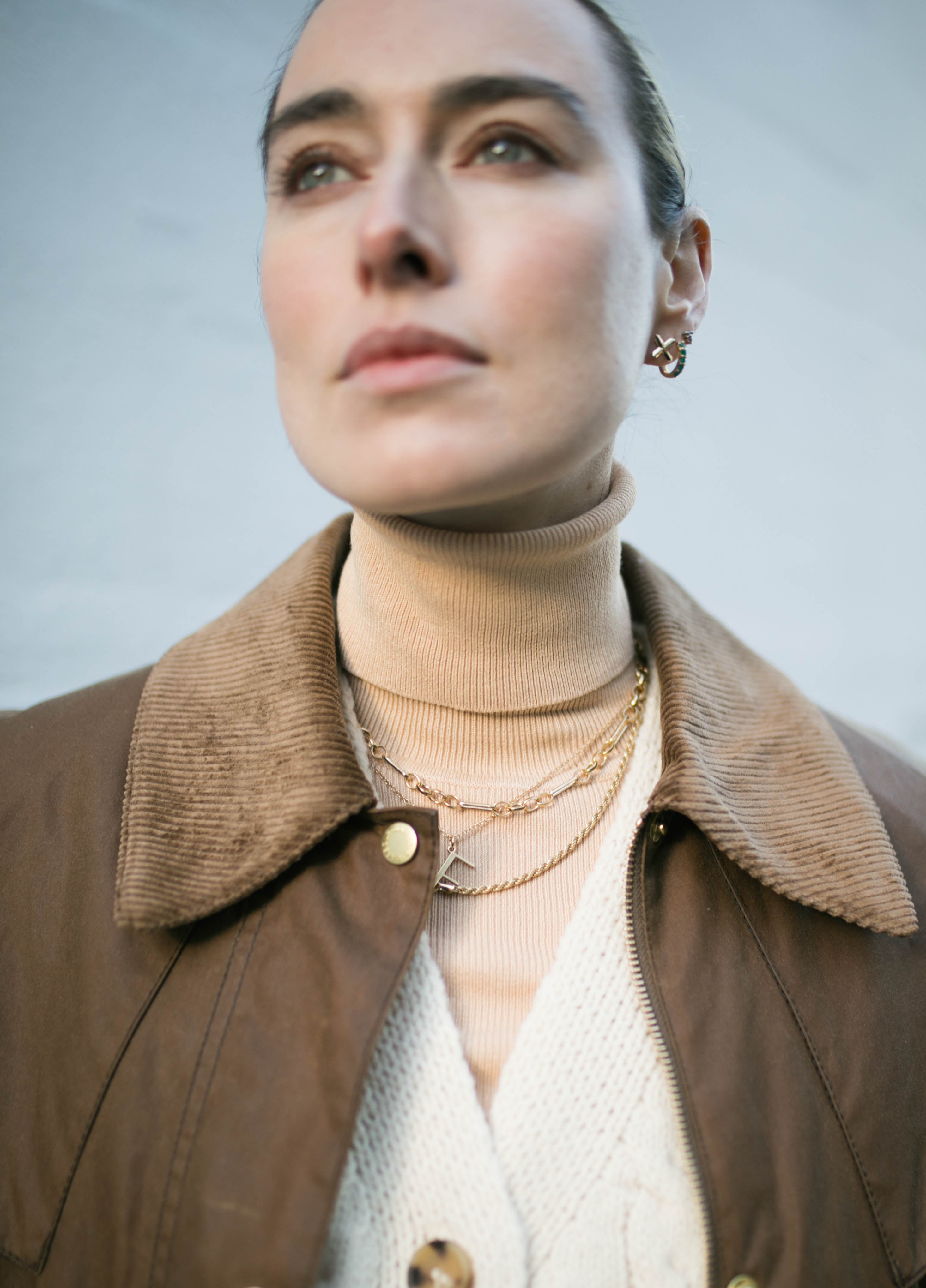 Model looking past camera wearing collared wax jacket and layered Antonia Guise gold vermeil necklaces including our Mary Figaro Chain Necklace