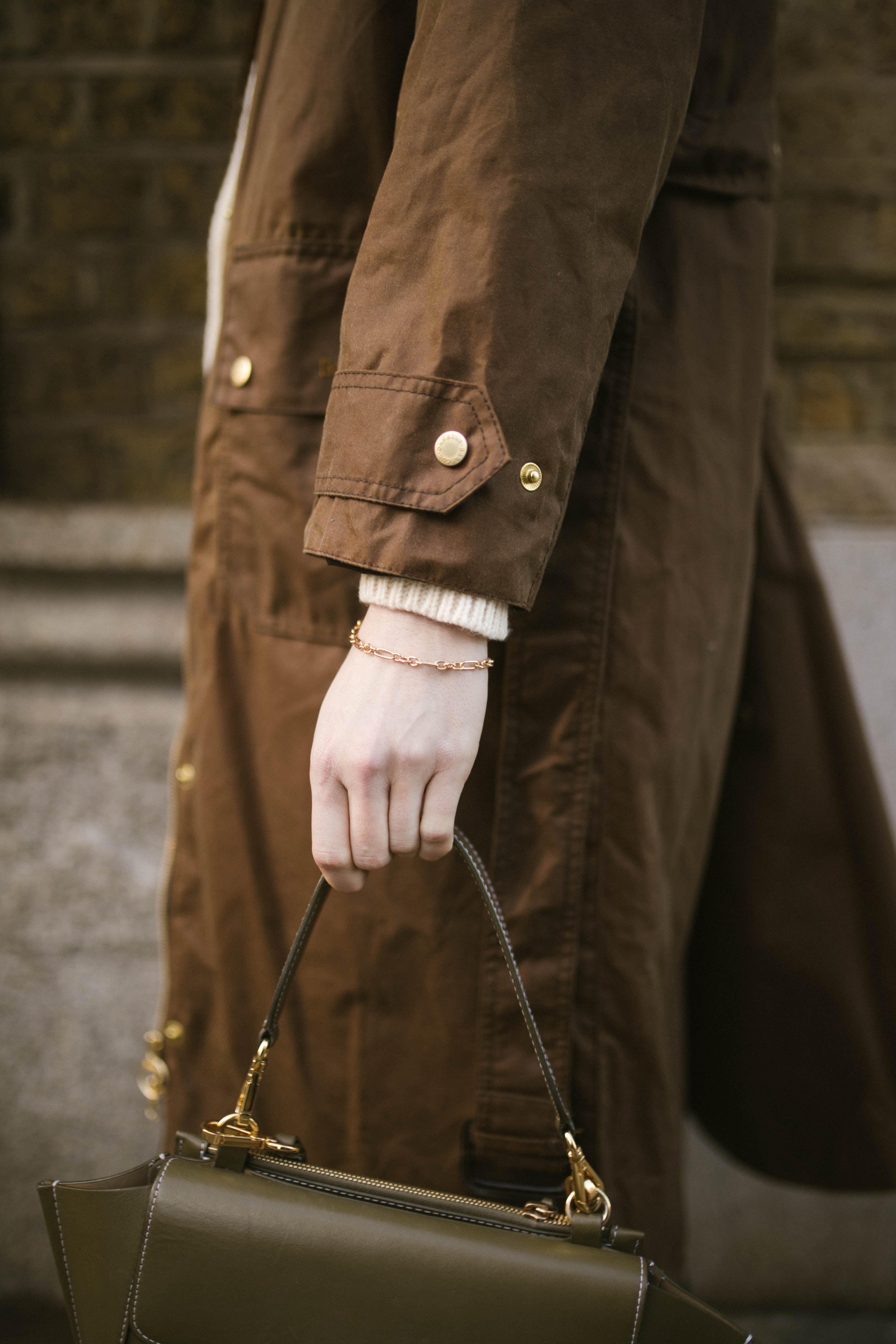 Model wearing brown wax jacket with green handbag and our gold chain Mary Bracelet 