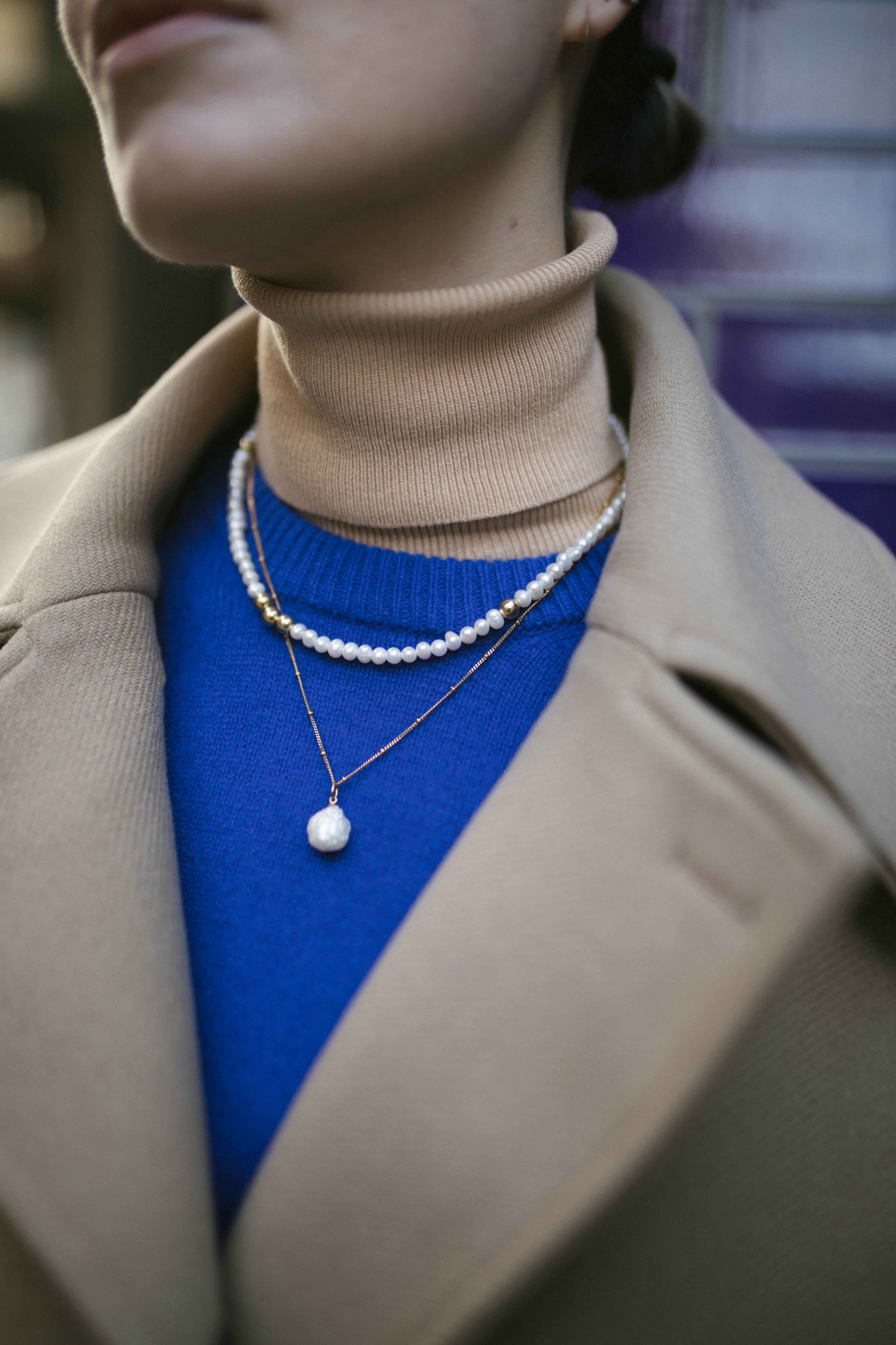 Model wearing blue jumper and camel coat along with our Anna Pearl Necklace and Grace Pearl Necklace