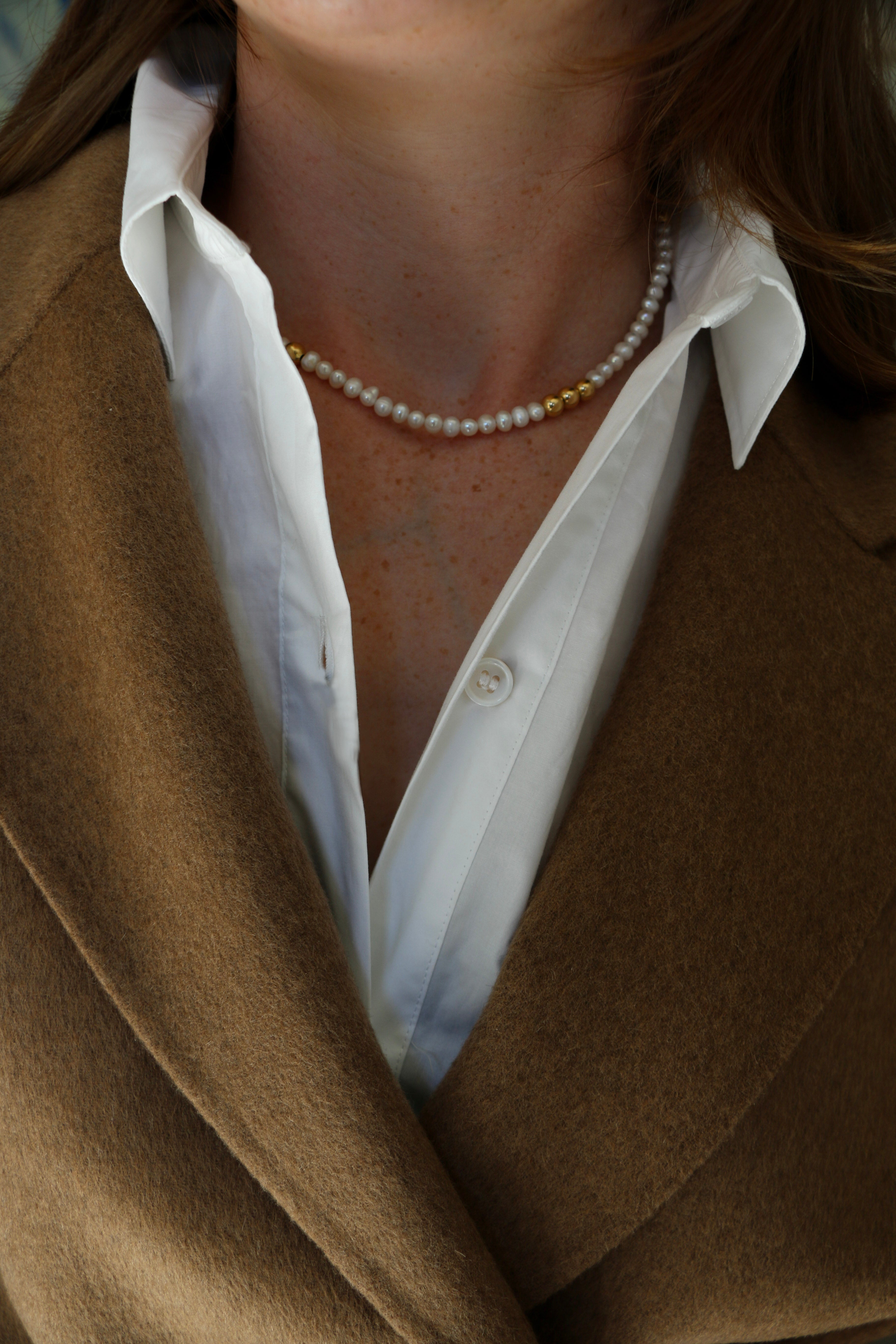 Close up of Grace Pearl Necklace on model wearing white shirt and camel wool coat