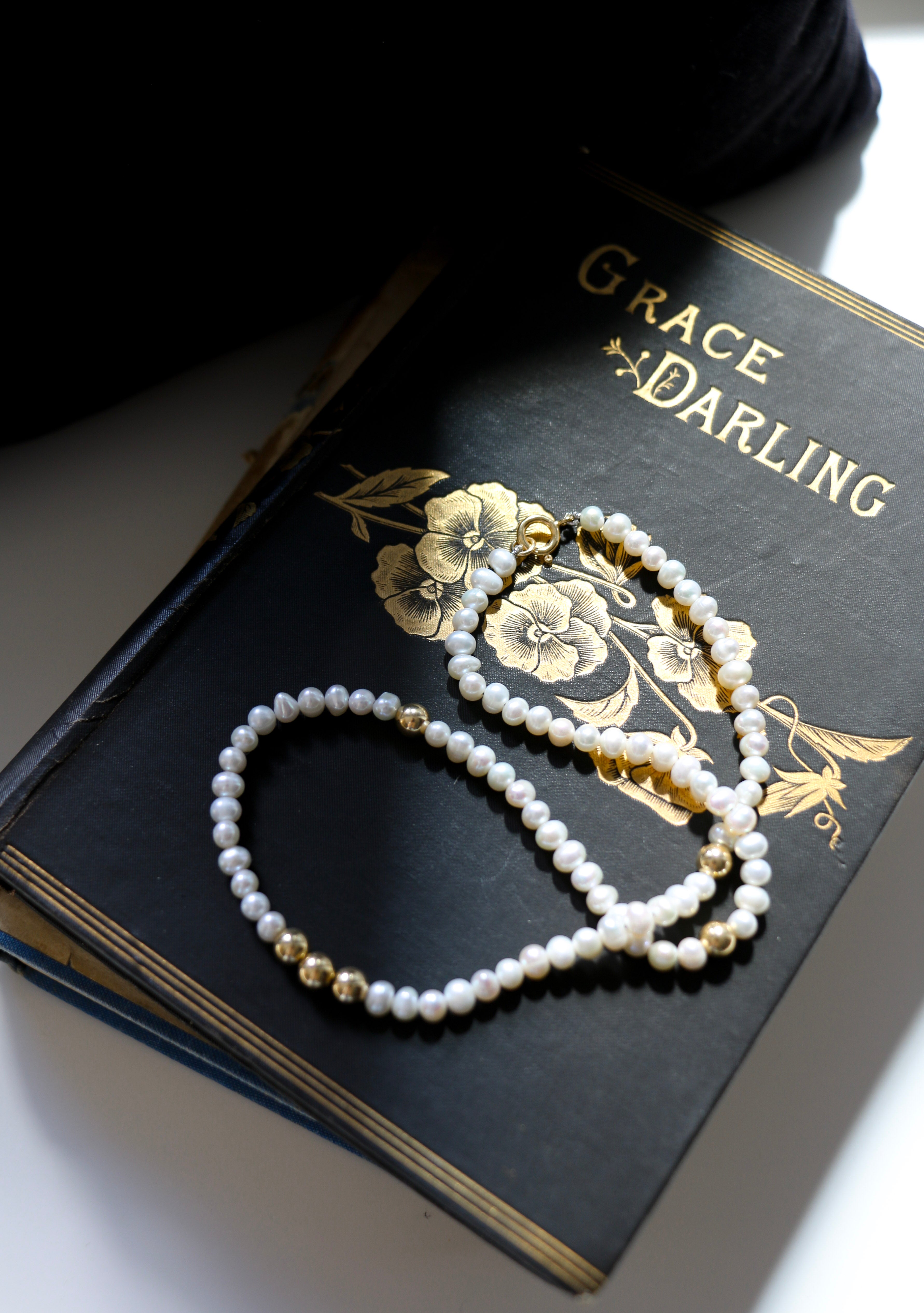 Grace Pearl Necklace lying on a book a out our muse Grace Darling