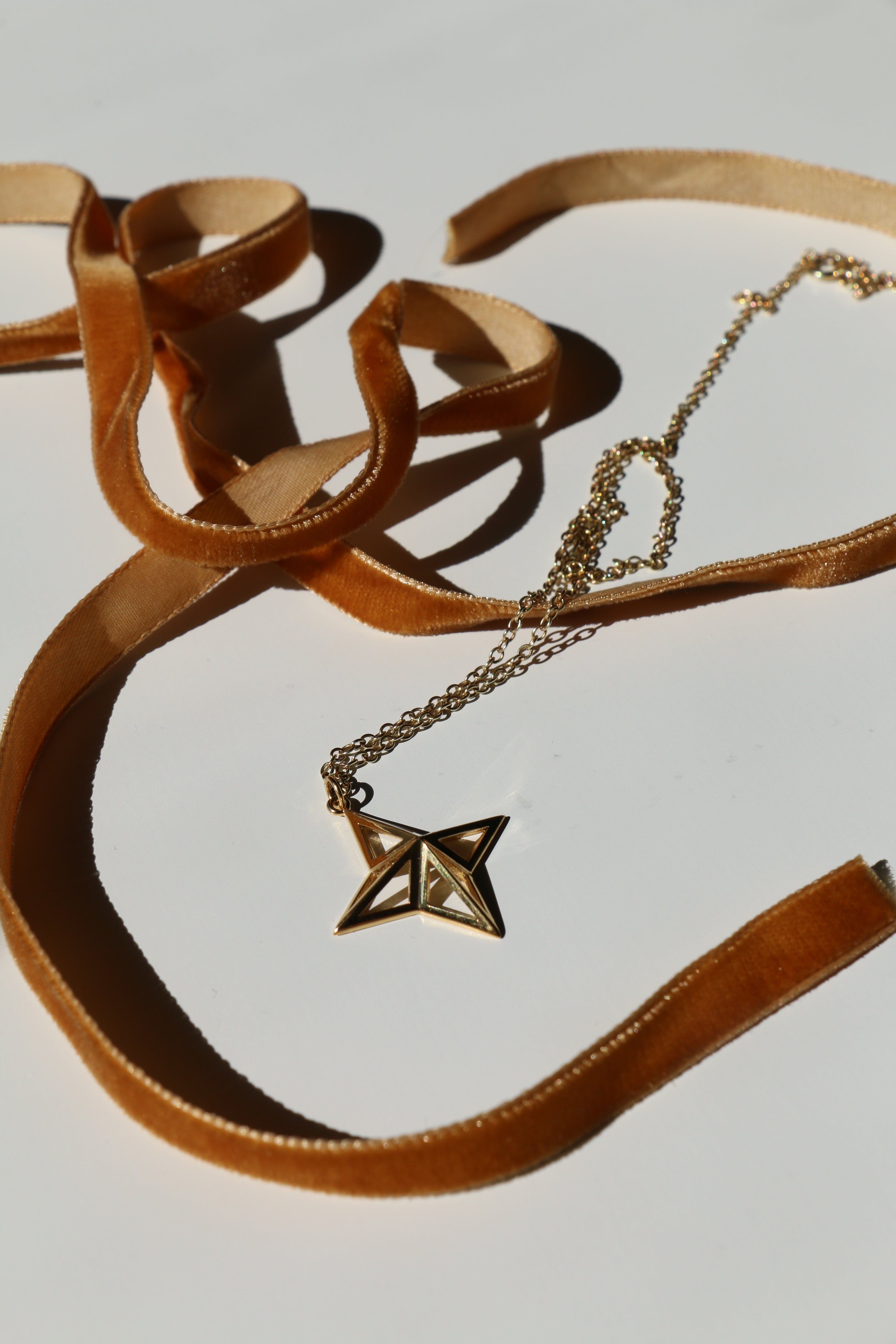 Theodora Gold Necklace on a white background with shadows and mustard velvet ribbon snaking around it