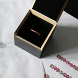 Image of oval Pink Ruby and round Diamond eternity band set in yellow gold in its  black recycled MDF presentation box on top of the original drawings