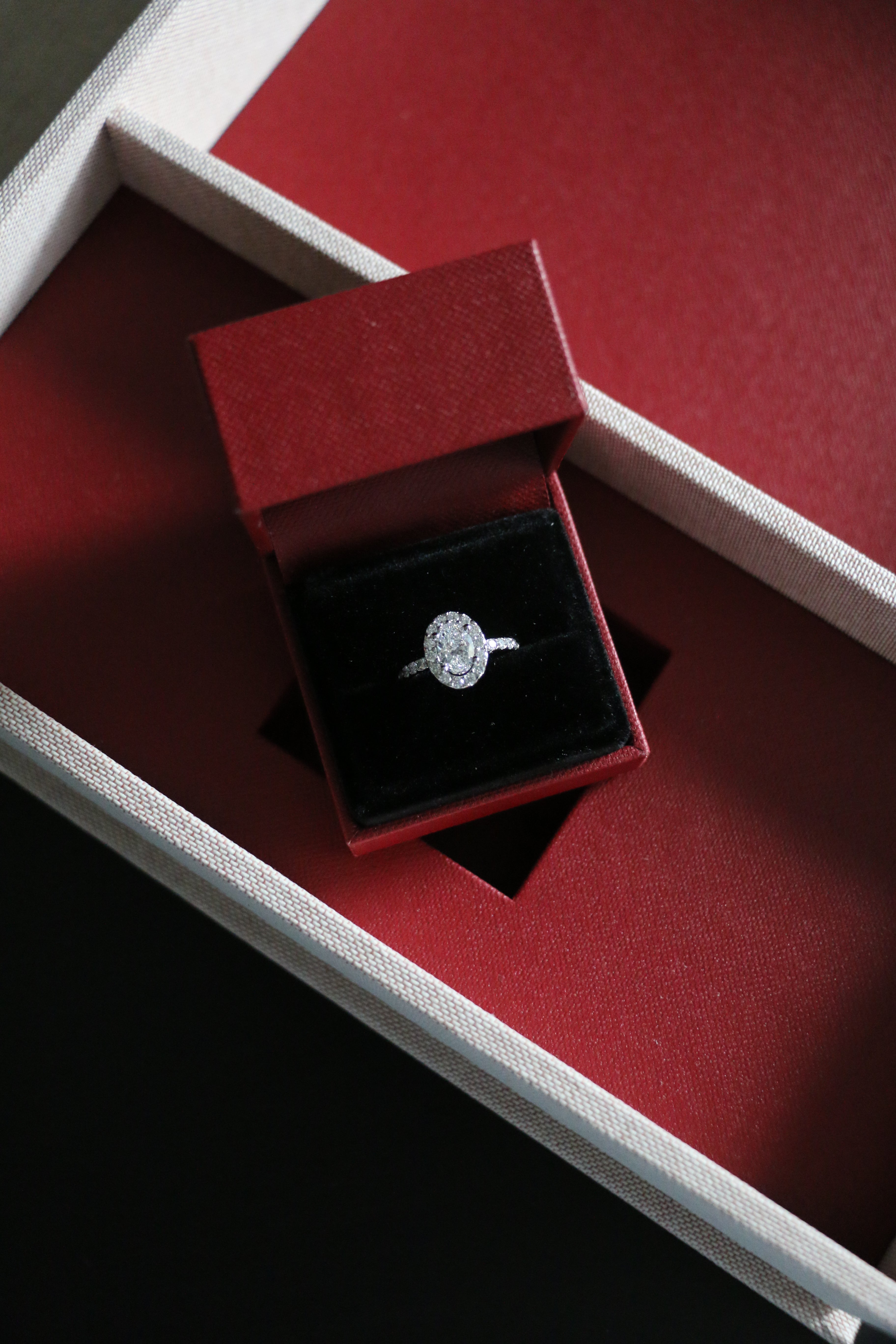 A totally bespoke platinum and diamond engagement ring, designed by Antonia Guise. Featuring a GIA certified oval diamond set in a diamond halo with diamond band detailing. In it's red presentation box. 