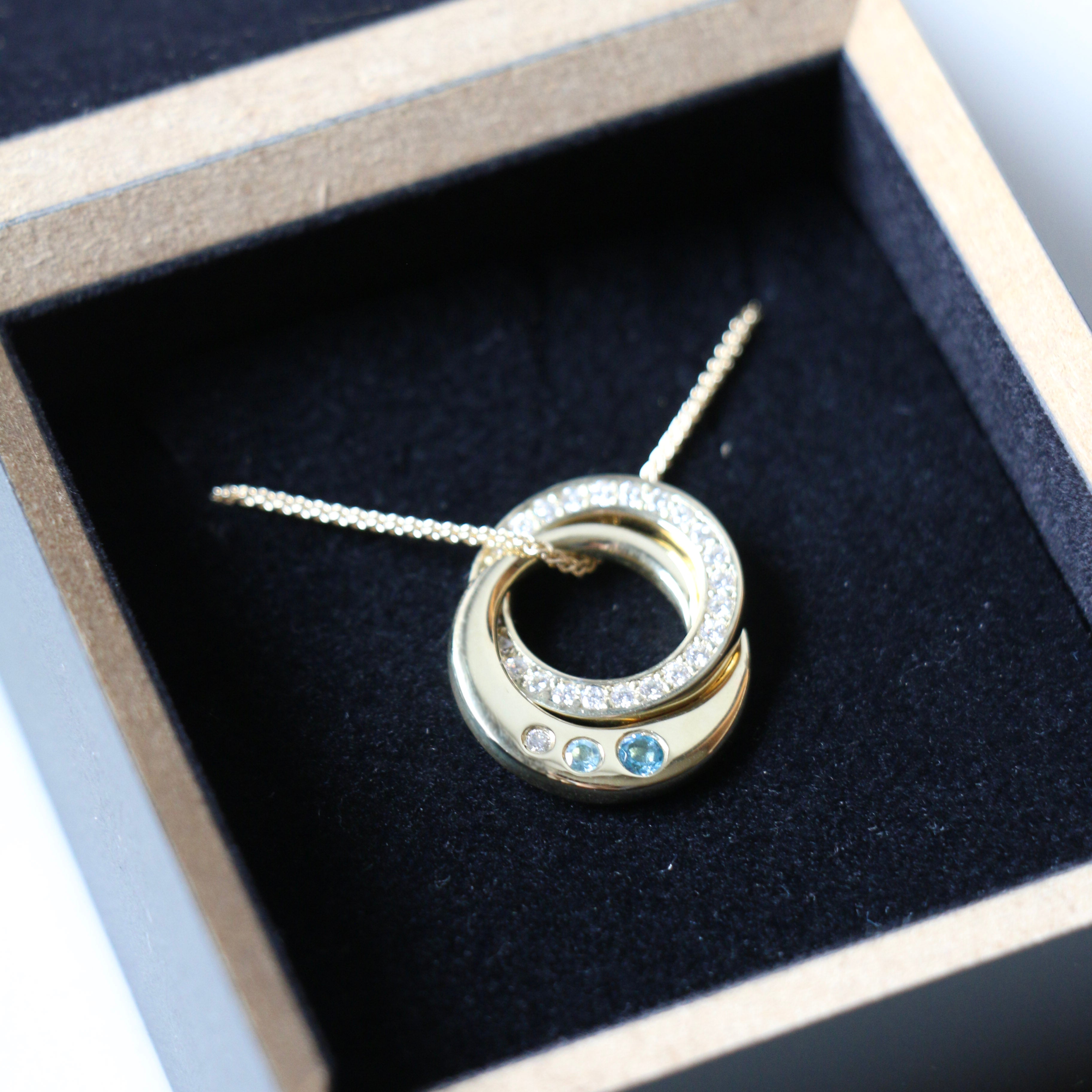 Interlocking diamond and topaz bespoke necklace lying in black presentation box