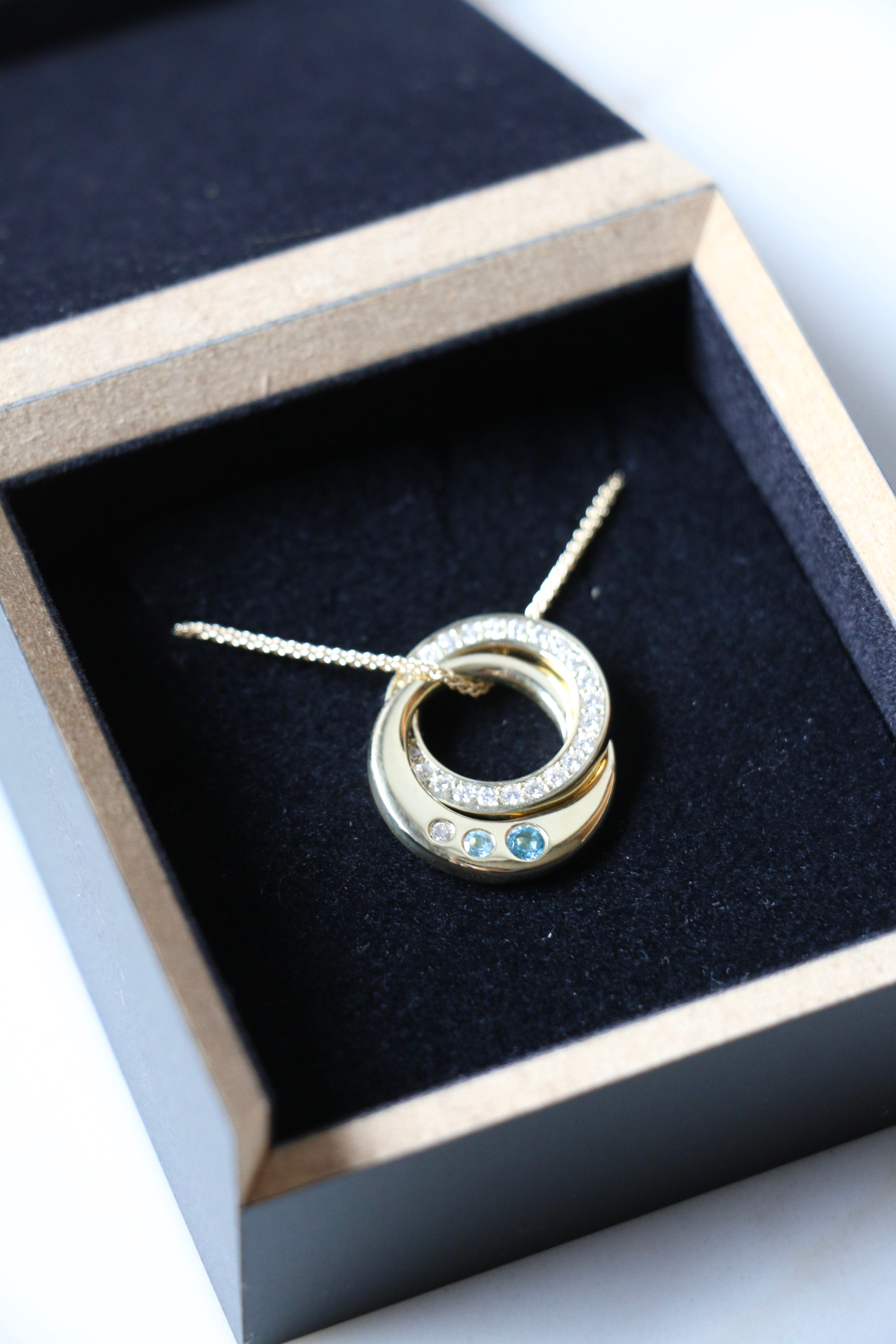 Interlocking diamond and topaz bespoke necklace lying in black presentation box
