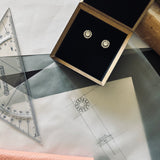 Pair of bespoke repurposed diamond halo studs in their black presentation box on top of the original sketches 