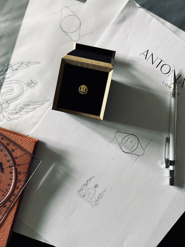 Image of signet ring in our presentation box sitting on Antonia's desk with hand drawn designs