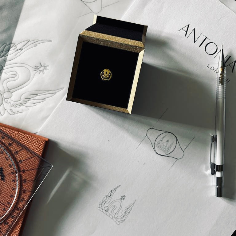 Image of signet ring in our presentation box sitting on Antonia's desk with hand drawn designs