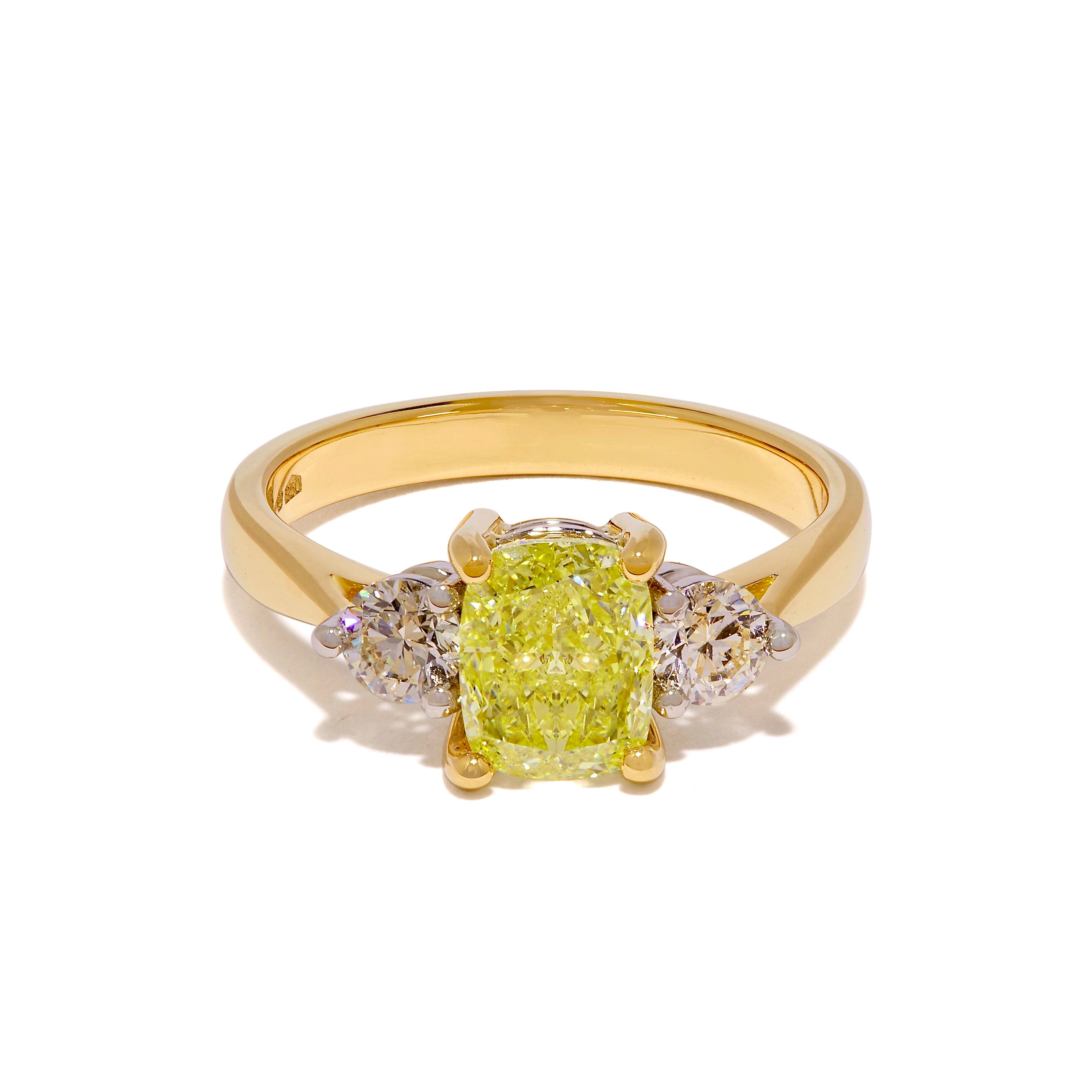 A Yellow diamond flanked by normal diamond trilogy ring in 18ct yellow gold lying on a white background