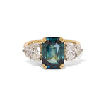 A unique unheated 6.06ct teal sapphire, elongated cushion cut centre stone, with 4  tapering diamond oval side stones. All set in recycled gold and platinum. Designed by London based engagement ring designer Antonia Guise.