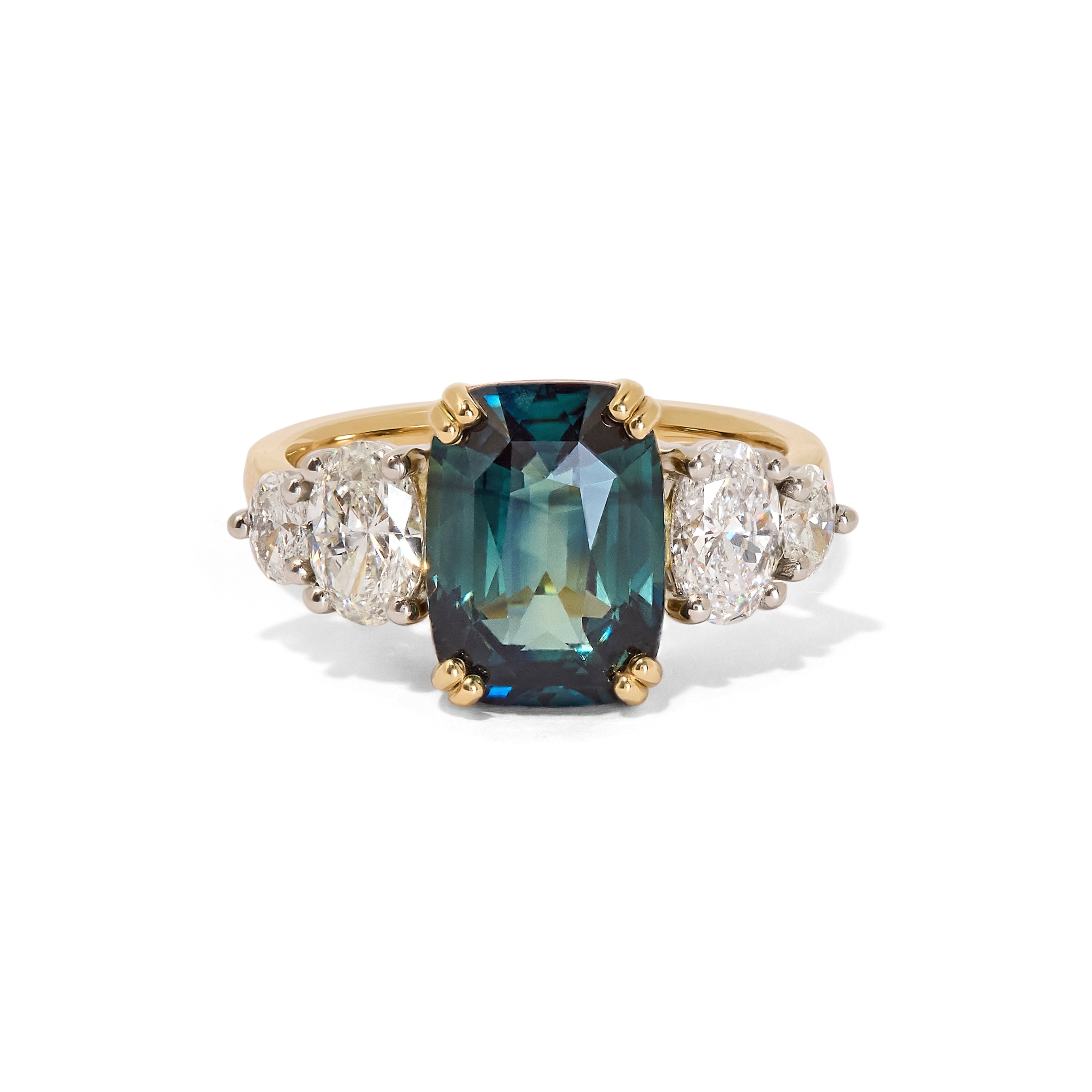 A unique unheated 6.06ct teal sapphire, elongated cushion cut centre stone, with 4  tapering diamond oval side stones. All set in recycled gold and platinum. Designed by London based engagement ring designer Antonia Guise.