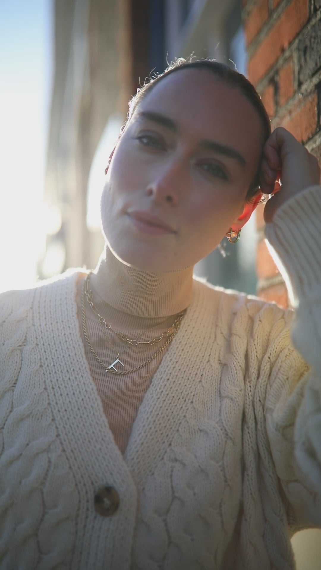 Backlit video of model wearing white chunky knit cardi and F anne initial with layered Antonia Guise Chains