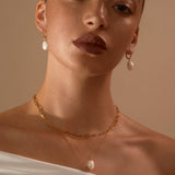 Model looking to camera wearing  Hedy pearl drop earrings and Anna + Jenny Layering set