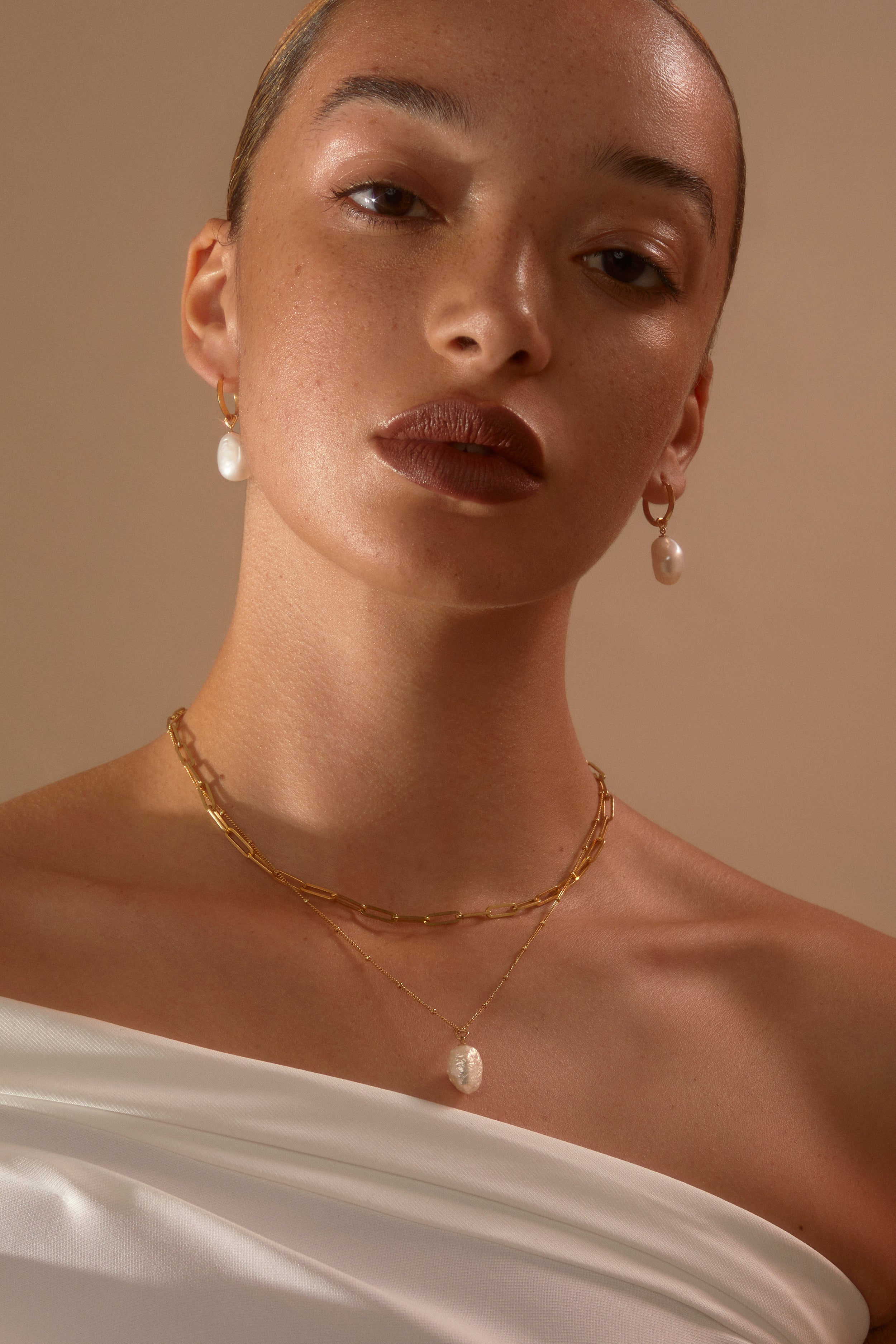 Model looking to camera wearing  Hedy pearl drop earrings and Anna + Jenny Layering set