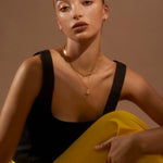 Model looking to camera wearing banana yellow trousers and a black top with the Antonia Guise Theodora necklace in gold vermeil and out Jenny Trace Chain