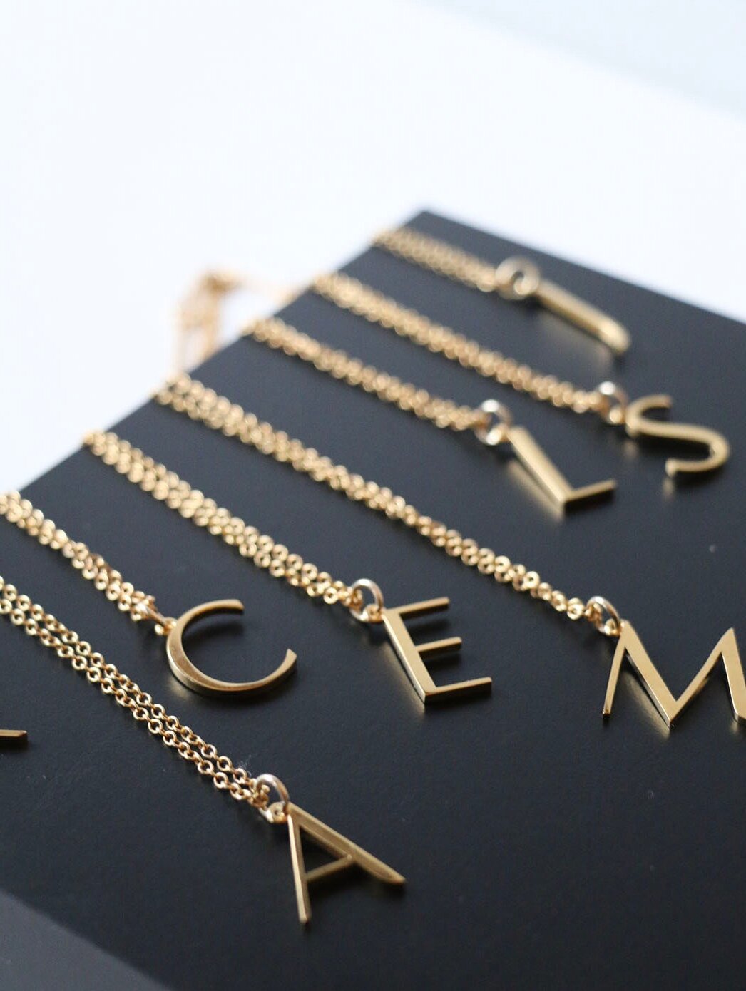 An assortment of initial necklaces laid out on a black background