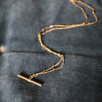 Our handmade in England, Gold Vermeil T-Bar Necklace lying on a blue velvet background